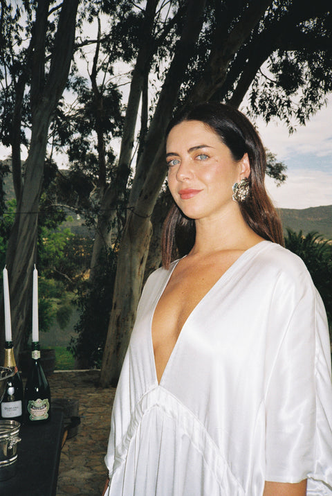 Woman in a white dress standing outdoors with trees and a clear sky in the background